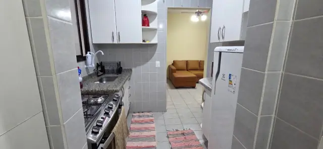 Cozinha com cooktop e geladeira, com o sofá da sala ao fundo