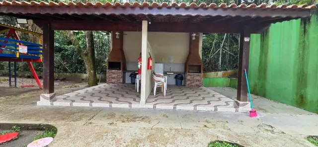 Espaço gourmet do condomínio com churrasqueira a carvão e playground ao fundo