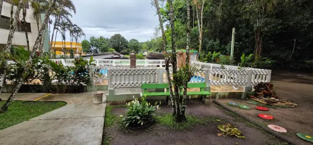Jardim do condomínio com bancos, canteiros e piscina ao fundo