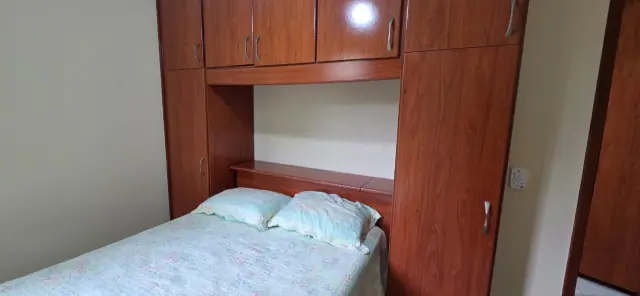 Quarto com cama de casal e guarda-roupa em madeira com mesa de trabalho