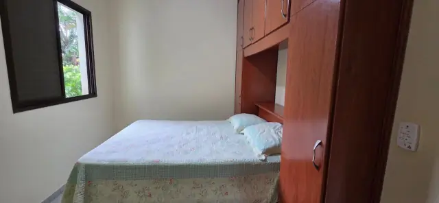 Quarto com cama de casal, guarda-roupa em madeira e janela com vista verde