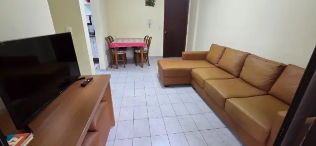 Sala de estar com sofá de couro caramelo, TV e mesa de jantar