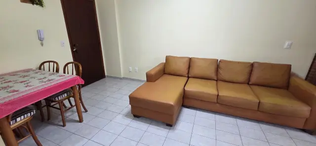 Sofá caramelo na sala ao lado da mesa de jantar com toalha florida