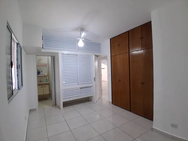 Suíte ampla com guarda-roupa embutido em madeira, ventilador de teto e banheiro privativo