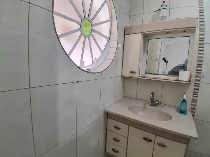 Banheiro da suíte com vitral redondo charmoso e gabinete com espelho