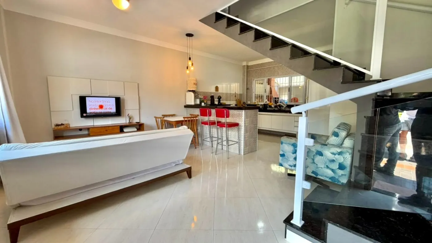 Sala integrada com escada em vidro e cozinha ao fundo